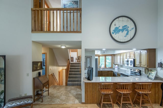 kitchen featuring light countertops, appliances with stainless steel finishes, a kitchen bar, and a towering ceiling