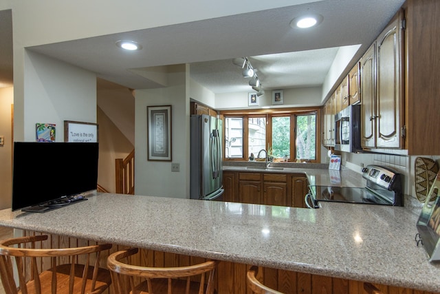 kitchen with brown cabinetry, a peninsula, a breakfast bar, a sink, and stainless steel appliances