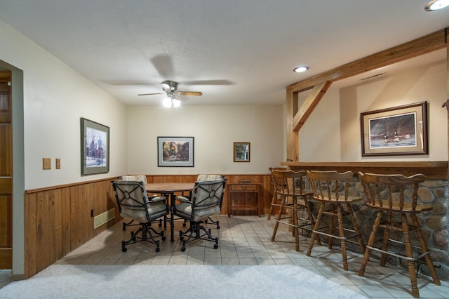 dining room featuring ceiling fan, visible vents, wainscoting, light tile patterned floors, and wooden walls
