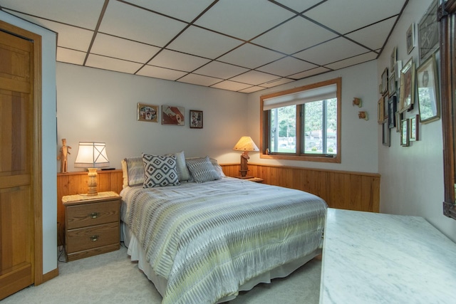 bedroom featuring wood walls, a drop ceiling, a wainscoted wall, and light carpet