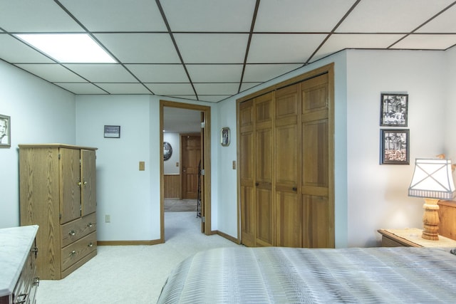 bedroom with baseboards, light colored carpet, a drop ceiling, and a closet