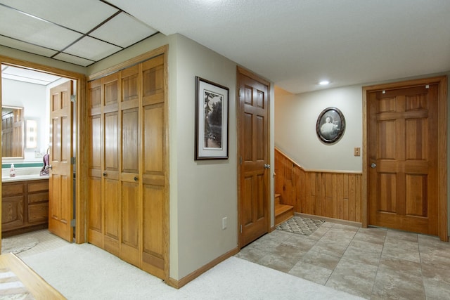 corridor featuring wooden walls, a wainscoted wall, and stairs