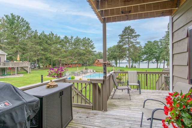 wooden deck with a water view, a yard, grilling area, and an outdoor pool