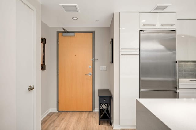 kitchen featuring white cabinets, visible vents, stainless steel built in refrigerator, and light wood-type flooring