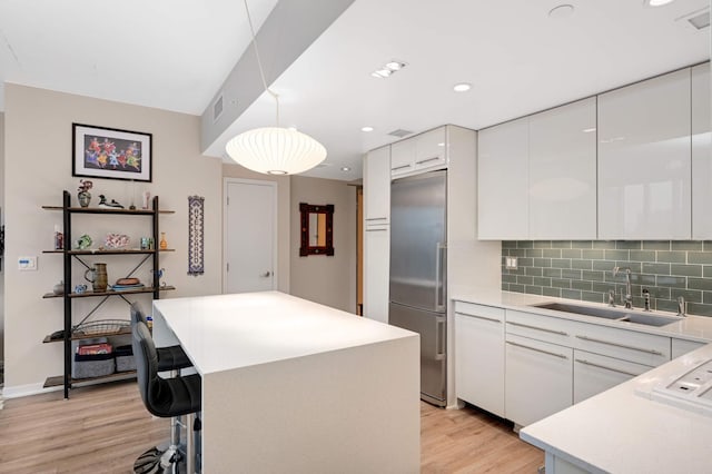 kitchen featuring a sink, light wood finished floors, white cabinetry, visible vents, and stainless steel built in refrigerator