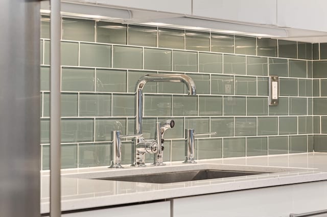 room details featuring white cabinets, decorative backsplash, and a sink