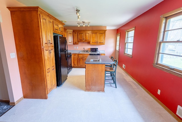 kitchen with an island with sink, a kitchen bar, brown cabinets, a sink, and black appliances