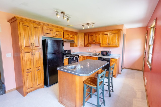 kitchen featuring a sink, baseboards, black appliances, under cabinet range hood, and an island with sink