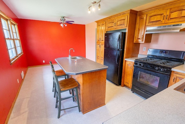 kitchen featuring ceiling fan, a sink, brown cabinetry, under cabinet range hood, and black appliances