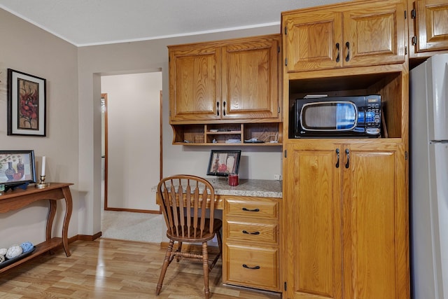 home office with crown molding, baseboards, built in desk, and light wood-style floors