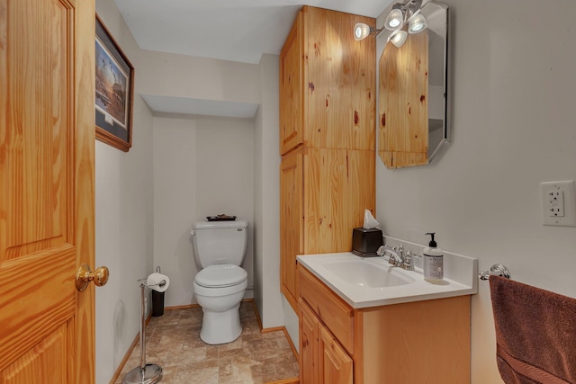 half bath with baseboards, stone finish floor, vanity, and toilet