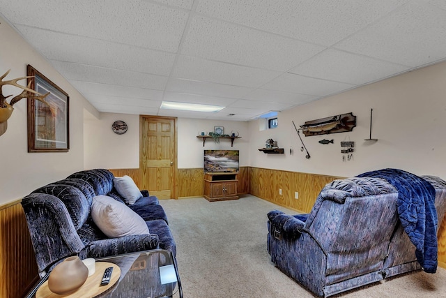 carpeted living area featuring wooden walls, a drop ceiling, and a wainscoted wall