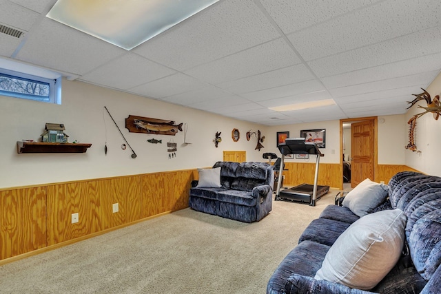 carpeted living area featuring wooden walls, wainscoting, a drop ceiling, and visible vents