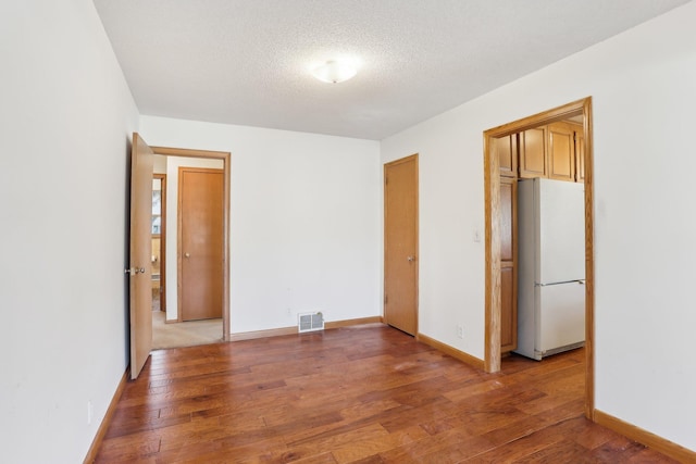 unfurnished bedroom with a textured ceiling, freestanding refrigerator, baseboards, light wood-type flooring, and visible vents