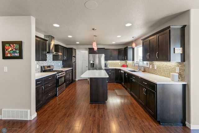 kitchen with a sink, stainless steel appliances, visible vents, wall chimney range hood, and a kitchen island