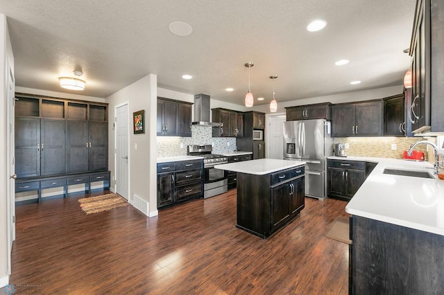 kitchen featuring a center island, a sink, backsplash, wall chimney range hood, and appliances with stainless steel finishes