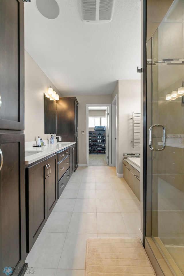 bathroom featuring a stall shower, double vanity, baseboards, and tile patterned flooring