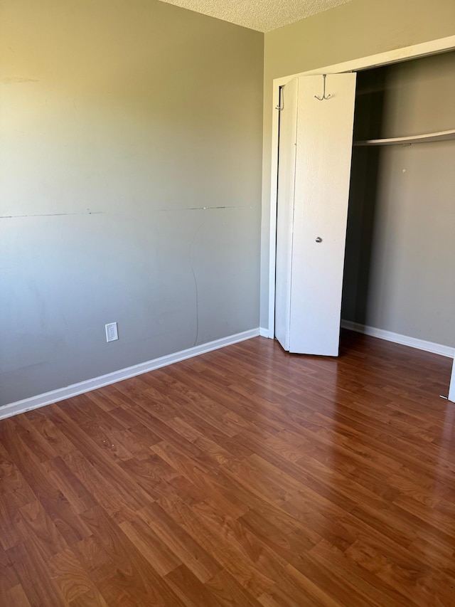 unfurnished bedroom featuring baseboards, a closet, dark wood-style flooring, and a textured ceiling