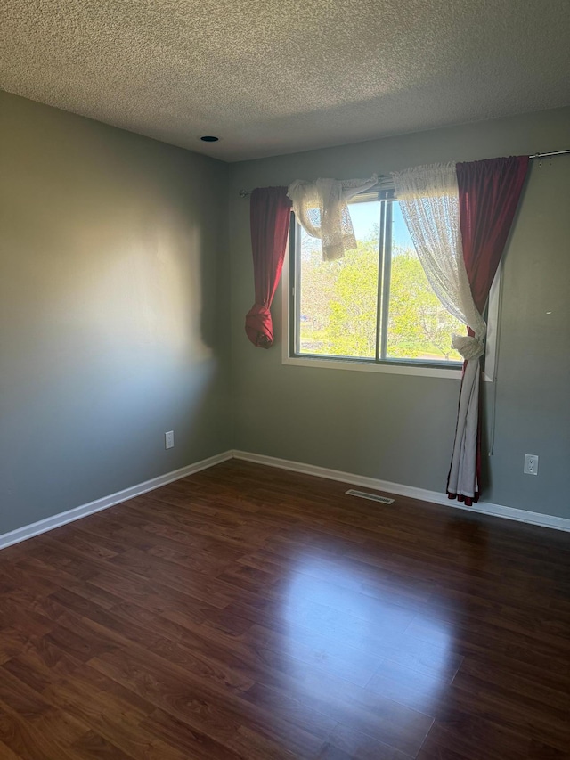 unfurnished room featuring visible vents, a textured ceiling, dark wood-style flooring, and baseboards