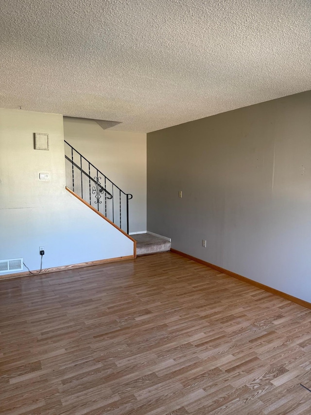 empty room with visible vents, stairs, a textured ceiling, and wood finished floors