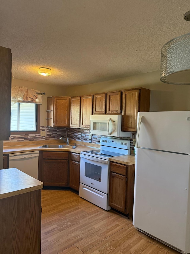 kitchen featuring a sink, brown cabinetry, white appliances, and a textured ceiling