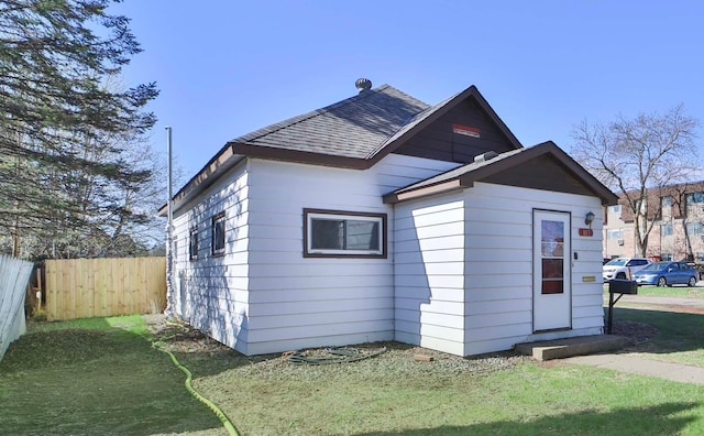 rear view of property with a shingled roof and fence