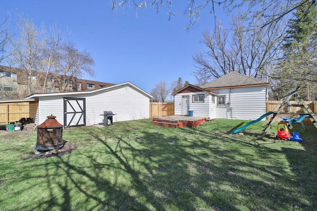 view of yard featuring an outdoor fire pit, a wooden deck, a fenced backyard, an outbuilding, and a playground
