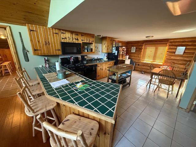 kitchen featuring rustic walls, stove, black microwave, a peninsula, and tile countertops