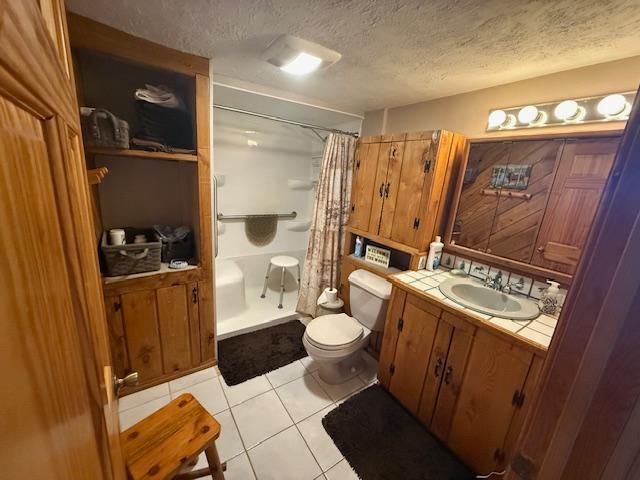 full bath featuring a textured ceiling, a shower with shower curtain, toilet, vanity, and tile patterned flooring