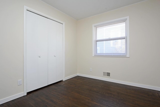 unfurnished bedroom featuring visible vents, dark wood finished floors, baseboards, and a closet