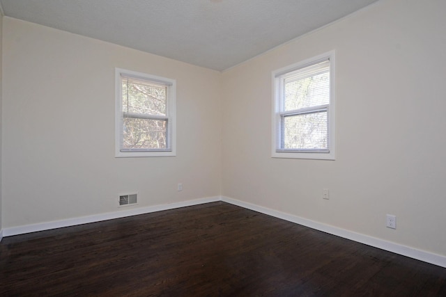 empty room featuring baseboards, dark wood finished floors, and visible vents