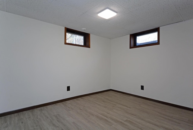 basement featuring baseboards, a paneled ceiling, wood finished floors, and a healthy amount of sunlight