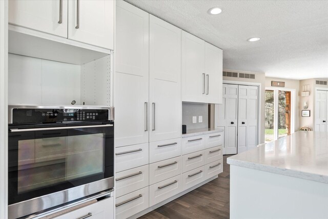 1206 Pinecrest Ln, New Richmond, WI 54017 - kitchen with stainless steel oven, a textured ceiling, white cabinets, dark wood finished floors, and light stone countertops