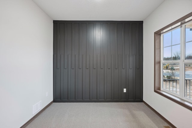 unfurnished room featuring light colored carpet, visible vents, a healthy amount of sunlight, and baseboards