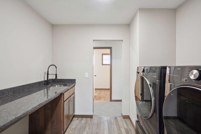 clothes washing area with cabinet space, washing machine and clothes dryer, a sink, baseboards, and light wood-type flooring