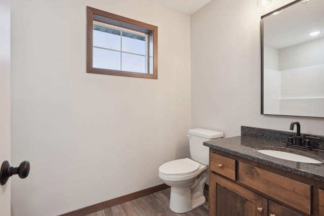 bathroom with toilet, vanity, wood finished floors, and baseboards