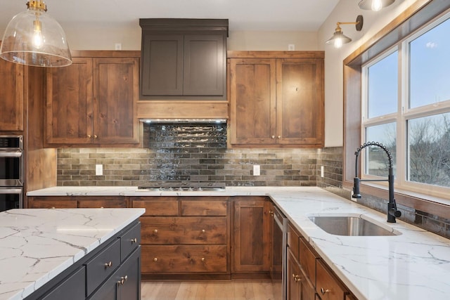 kitchen featuring light wood finished floors, a sink, stainless steel appliances, tasteful backsplash, and light stone counters