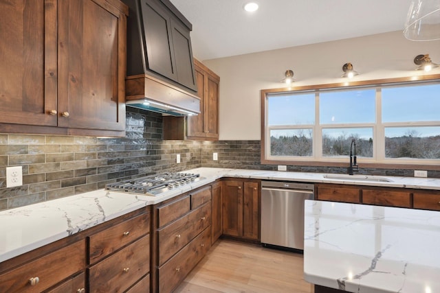 kitchen with appliances with stainless steel finishes, light wood-type flooring, light stone countertops, and a sink