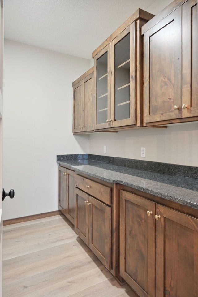kitchen with dark stone counters, light wood finished floors, glass insert cabinets, and baseboards