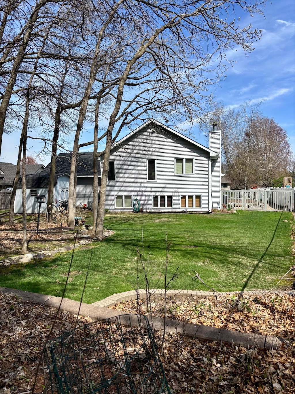 rear view of house featuring a lawn, fence, and a chimney