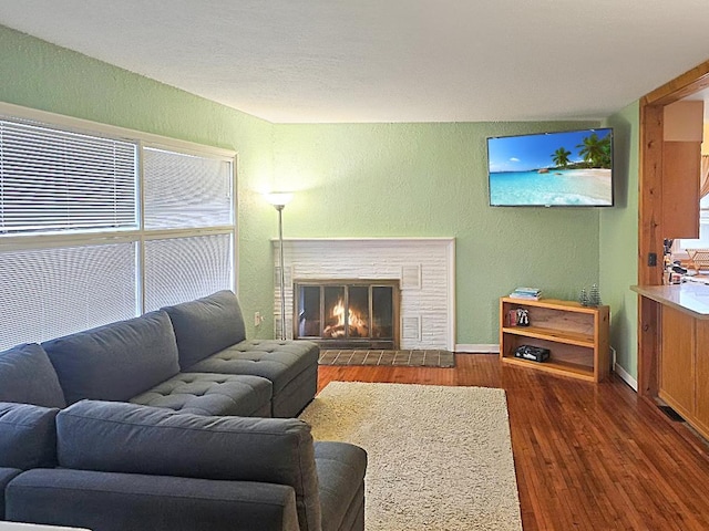 living room with baseboards, a textured wall, a glass covered fireplace, and wood finished floors