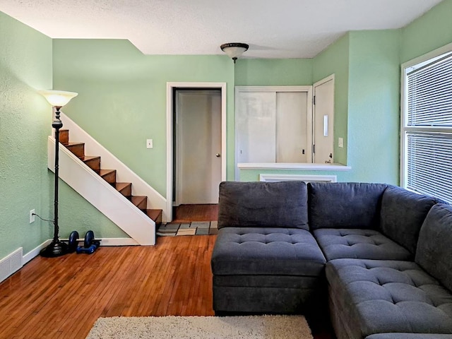 living area with a textured wall, baseboards, wood finished floors, visible vents, and stairway