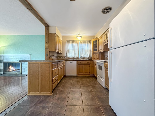 kitchen with a sink, white appliances, a glass covered fireplace, a peninsula, and visible vents