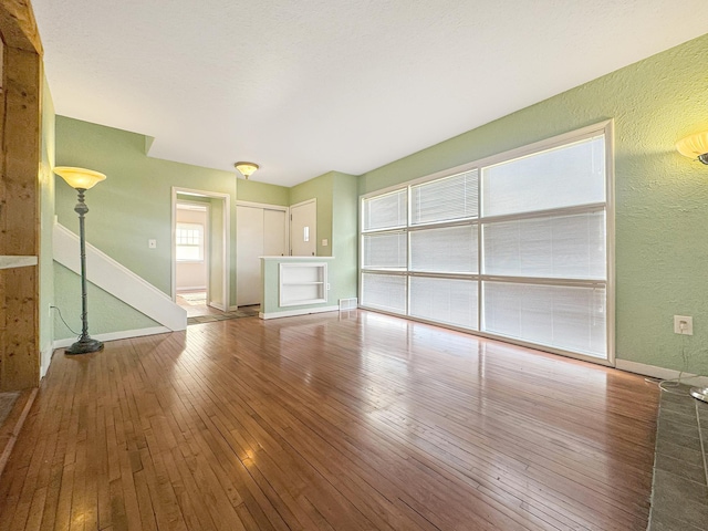 unfurnished living room featuring wood-type flooring, baseboards, and a textured wall