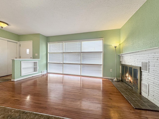 unfurnished living room with a textured ceiling, a textured wall, hardwood / wood-style flooring, and a stone fireplace