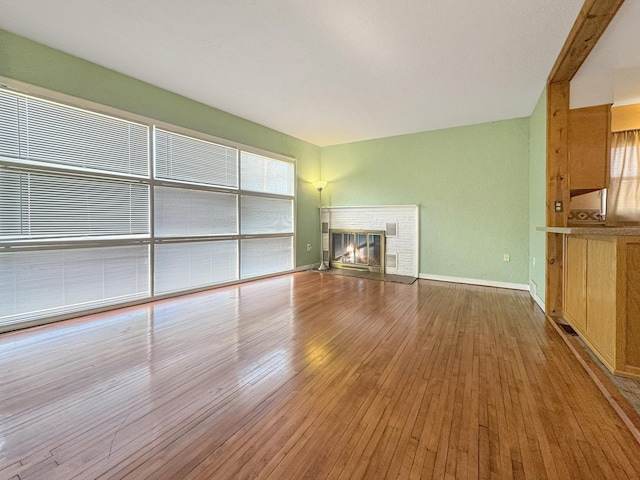 unfurnished living room with baseboards, a glass covered fireplace, and hardwood / wood-style flooring