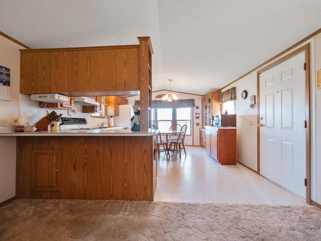 kitchen with a peninsula, brown cabinets, vaulted ceiling, under cabinet range hood, and a notable chandelier