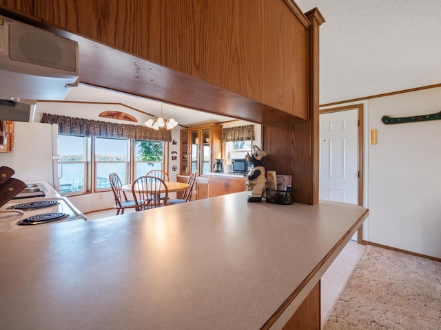 kitchen with freestanding refrigerator, brown cabinetry, range hood, decorative light fixtures, and a chandelier