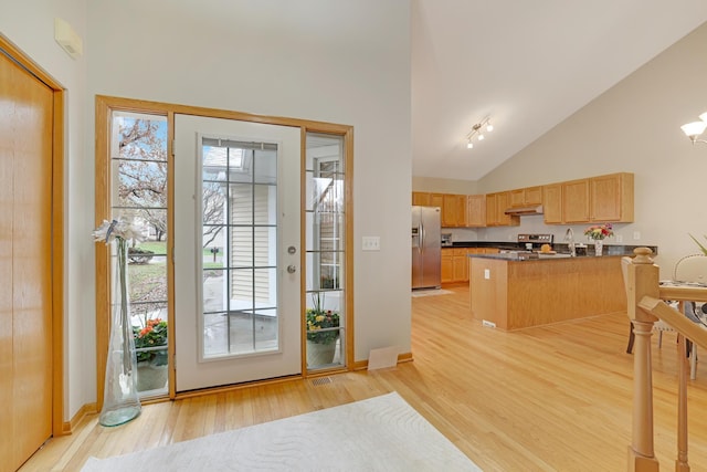 interior space with light wood-style flooring, stainless steel appliances, under cabinet range hood, dark countertops, and a peninsula