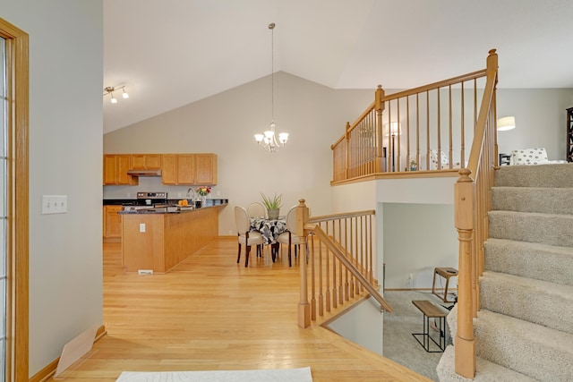 kitchen featuring stainless steel electric stove, light wood-style floors, under cabinet range hood, a peninsula, and a notable chandelier